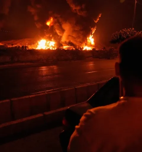 A man looks at flames rising from an oil storage facility after it appeared to have been struck by an Israeli attack, in Tehran, Iran, early Sunday, June 15, 2025