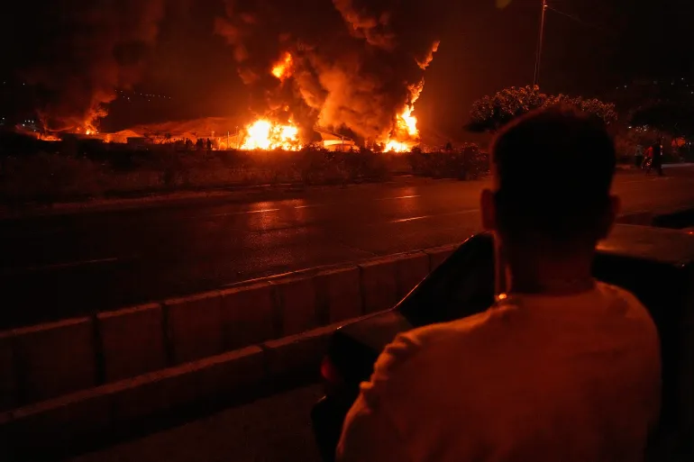 A man looks at flames rising from an oil storage facility after it appeared to have been struck by an Israeli attack, in Tehran, Iran, early Sunday, June 15, 2025