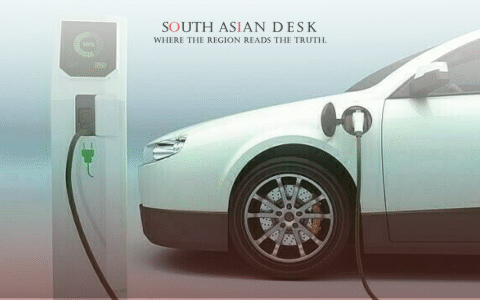 A white electric vehicle connected to a charging station with a cable, displaying a charge level on the station's screen.