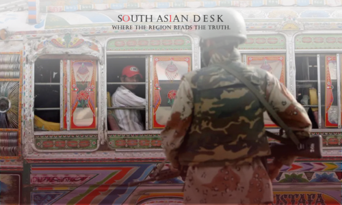 A soldier in camouflage and helmet stands guard in front of a brightly decorated bus with colorful patterns and designs, with a person visible inside.