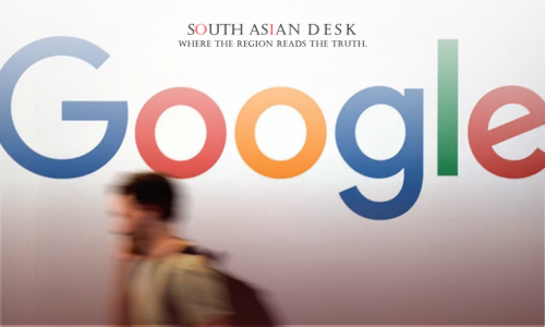 A large Google logo with multicolored letters on a white wall, with a blurred person walking in front carrying a backpack.