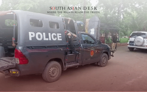 A police truck with 'POLICE' written on the side, parked on a dirt road with officers exiting, surrounded by trees and a gated area, with another vehicle in the background.