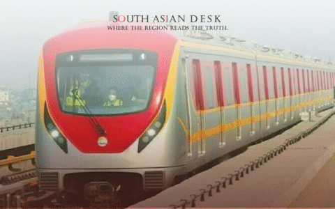 A modern red and silver metro train with yellow accents traveling on an elevated track, with a person in a high-visibility vest visible in the front window.