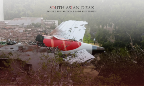 The wreckage of an aircraft with a red, white, and black tail section crashed into a ruined building, surrounded by debris and trees.