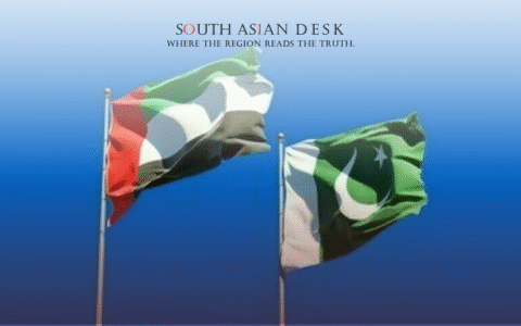 Two flags, the United Arab Emirates flag with green, white, black, and red vertical stripes, and the Pakistan flag with green and white with a crescent moon and star, waving against a clear blue sky.