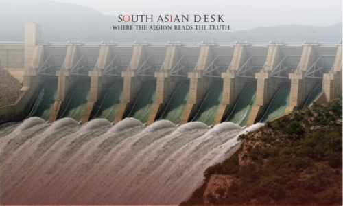 A large dam with multiple spillways releasing water, surrounded by hilly terrain and greenery.