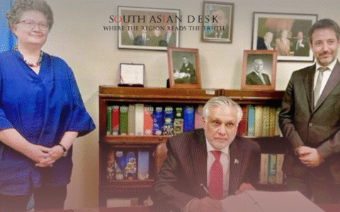 A woman in a blue outfit and two men in suits standing in an office with a bookshelf, framed photos, and a flag in the background, with one man signing a document.