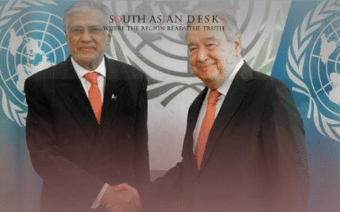 Two men in suits shaking hands in front of UN flags and a backdrop with the UN logo.