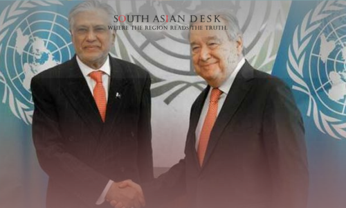 Two men in suits shaking hands in front of UN flags and a backdrop with the UN logo.