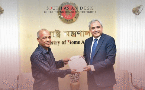 Two individuals in a formal setting, exchanging a decorative plate, with a backdrop featuring the emblem and text of the Ministry of Home Affairs in Bengali.