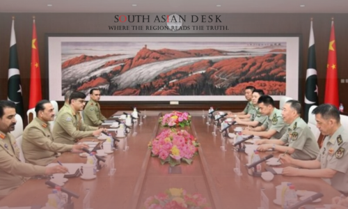 A formal meeting with individuals in military uniforms seated around a long table, decorated with flowers, with Pakistani and Chinese flags in the background and a large landscape painting on the wall.