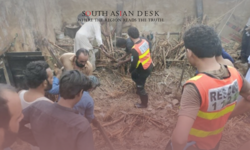 Rescue workers in orange vests labeled "RESCUE 1122" assisting people amidst debris and wooden structures of roof collapse in a muddy area.