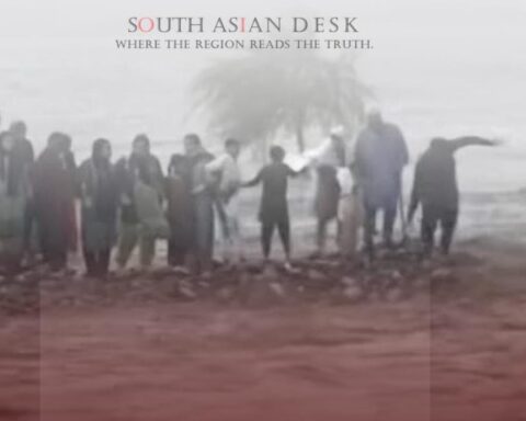 A group of people standing on a small elevated area surrounded by floodwater, with a tree in the background and a cloudy sky.