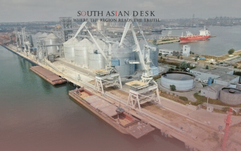 An aerial view of an industrial port facility with large grain silos, cranes, and a barge docked along a waterway, in constanta port