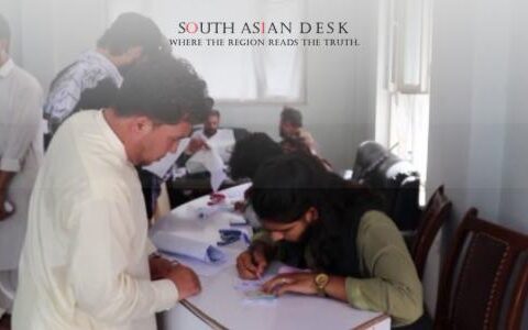 people registering at a desk inside a bright room, filling out documents.