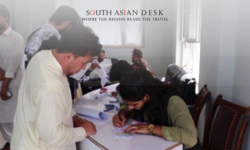 people registering at a desk inside a bright room, filling out documents.
